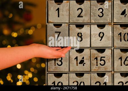 adventskalender.Geschenke und Überraschungen für Weihnachten und Neujahr.Retro Adventskalender und Kinderhand auf Lichter Girlanden Hintergrund.Hand öffnet die Stockfoto