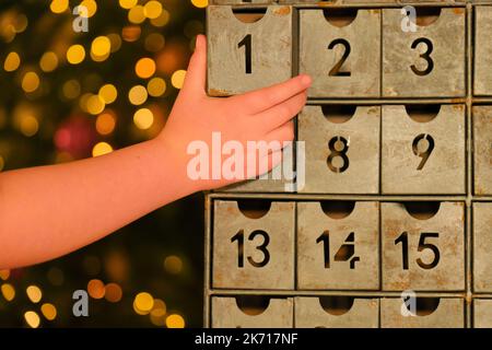 Retro Adventskalender und Kinderhand auf verschwommenem Licht Girlanden Hintergrund.Hand öffnet den Adventskalender. Traditionen und Symbole.Geschenke und Stockfoto