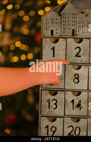 adventskalender im Vintage-Stil und Kinderhand auf Girlanden-Hintergrund. Traditionen und Symbole.Geschenke und Überraschungen zu Weihnachten und Neujahr Stockfoto