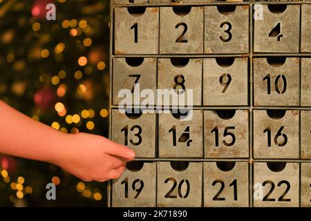 adventskalender Metallische und Kinderhand auf Lichtern Girlanden Hintergrund.Hand öffnet den Adventskalender. Traditionen und Symbole.Geschenke und Überraschungen für Stockfoto