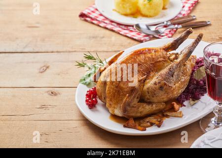 Von oben leckeres Perlhuhn mit Sauerkraut serviert auf Teller neben Glas Becher Rotwein auf Holz während des Mittagessens Stockfoto