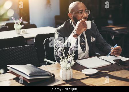 Ein Porträt eines reifen kahlen afrikanischen Geschäftsmannes mit Bart, in einer Brille, in einem formellen Anzug mit Krawatte, in einem Café im Freien sitzend und Nein machend Stockfoto
