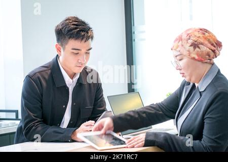 Zwei asiatische Geschäftsleute arbeiten zusammen und betrachten Tablets im Büro. Stockfoto