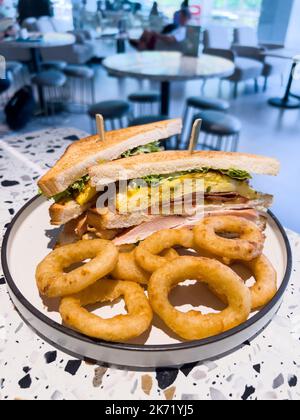 Vertikale Ansicht eines großen Club-Sandwiches mit mariniertem Huhn, putenspeck, Schinken, Rührei und Zwiebelringen als Beilage. Stockfoto