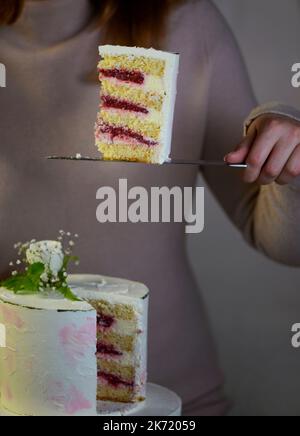 Das Mädchen schneidet und serviert ein Stück Kuchen. Festliche Hochzeit zweistufiger Kuchen mit frischen Blumen dekoriert Stockfoto