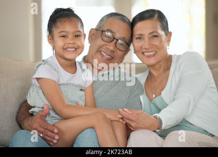 Ich war am liebsten bei meinen Großeltern. Ein älteres Paar, das zu Hause mit seiner Enkelin auf dem Sofa sitzt. Stockfoto