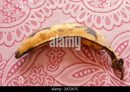 Auf einer rot-weißen Tischdecke befindet sich ein gepunkteter gelber, reifer Kochbanan. Stockfoto