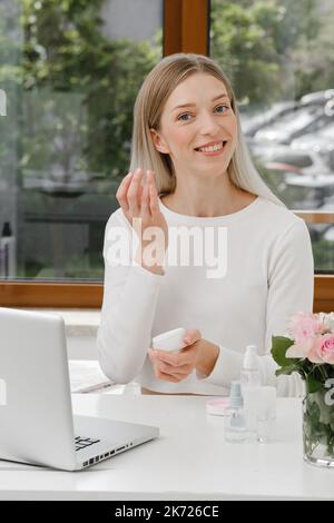 Anwendung Creme auf Schönheit blogger Gesicht in der Nähe von Laptop. Frau, die Online-Video-Inhalte macht, Live-Broadcast-Bewertung über kosmetische Produkte. Kosmetologie-Kurs Stockfoto