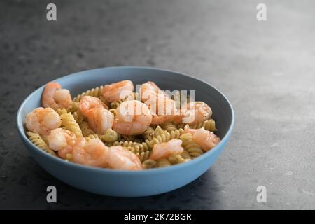 Fusilli mit Garnelen und Pesto in einer blauen Schale auf Betongrund, flacher Fokus Stockfoto