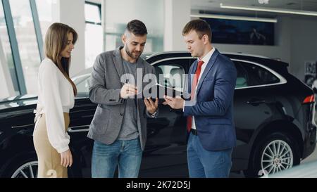 Hübscher junger Kerl unterzeichnet Verkauf und Kaufvertrag im Autohaus Stockfoto