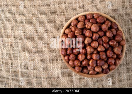 Draufsicht auf eine Schüssel voller Haselnüsse, auf Sackleinen Stockfoto