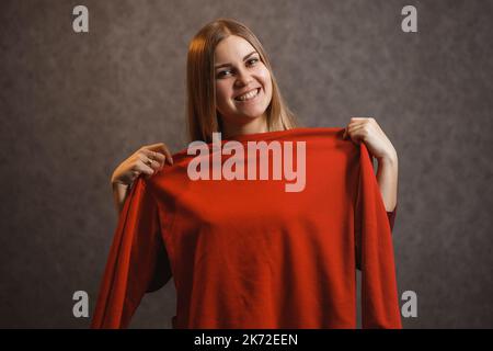 Schönes Mädchen versucht auf einem roten Pullover Stockfoto