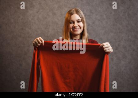 Schönes Mädchen versucht auf einem roten Pullover Stockfoto