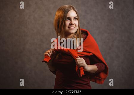 Mädchen versucht auf einem roten Pullover auf einem grauen Hintergrund Stockfoto