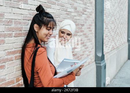 Multiethnische Freundinnen lächeln, während sie gemeinsam im Freien studieren. Stockfoto