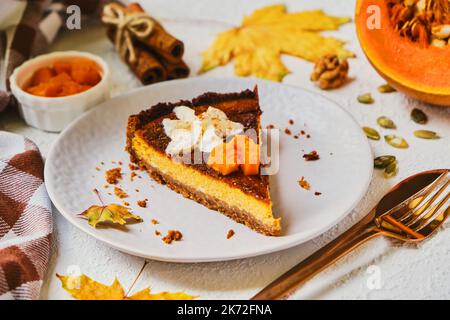 Hausgemachter Kürbis-Käsekuchen mit Schlagsahne auf grauem Teller dekoriert. Stockfoto