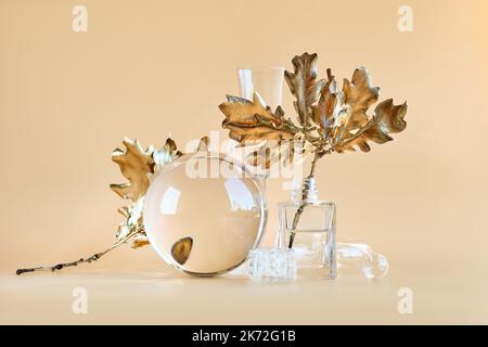 Biophiler Herbsthintergrund. Vergoldete Eichenblätter aus Gold, verzerrt durch durchsichtige Glasgläser, kleine Flaschen. Einfarbig orange beige erdefarben floral Stockfoto