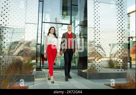 Respektabler Geschäftsmann und modische asiatische Geschäftsfrau, die in der Nähe des Büros läuft. In voller Länge zuversichtlich und erfolgreiche Paar in Business Casual Tuch Stockfoto