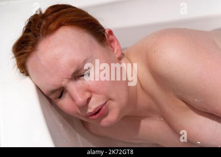 Eine Schwangere mit Kontraktionsschmerzen, die während der frühen Wehen in einem warmen Bad zu Hause auf ihrer Seite liegt Stockfoto