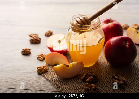 Einmachglas mit Honig Honig Dipper rote Äpfel und Walnüsse auf Küchentisch Stockfoto