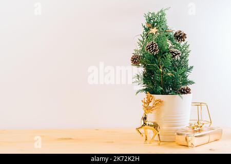 Kreativer natürlicher Miniatur-Weihnachtsbaum im Topf auf Holztisch mit Geschenkboxen und weißem Hintergrund. Weihnachtskarte mit Kopierplatz. Frohes Neues Stockfoto