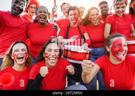 Multirassische rote Sportfans, die beim Unterstützen ihres Teams kreischen - Fußballfans, die Spaß an der Wettkampfveranstaltung haben - konzentrieren sich auf das Gesicht des Mädchens in der Mitte Stockfoto