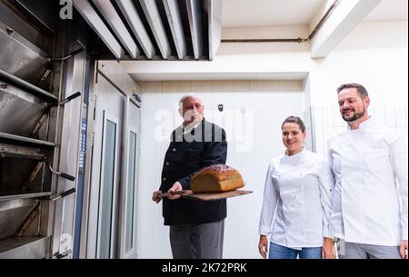 Lengerich, Deutschland. 17. Oktober 2022. Karl-Josef Laumann (CDU), Minister für Arbeit, Gesundheit und Soziales des Landes Nordrhein-Westfalen, nimmt mit einem Stopfer ein Brot aus dem Ofen. Rechts sind die Bäckermeister Christian und Pascal Klinker. Der Arbeitsminister besucht die Bäckerei und tauscht sich über die hohen Energiekosten und die Sicherung von Fachkräften aus. Die Bäckerei existiert seit 1911 und beliefert ihre fünf Fachgeschäfte, Schulen, Kindergärten, Seniorenheime und Restaurants mit Backwaren. Quelle: Guido Kirchner/dpa/Alamy Live News Stockfoto