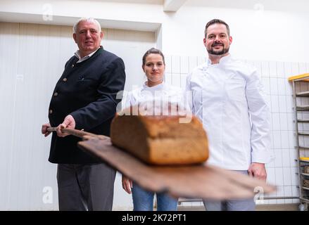 Lengerich, Deutschland. 17. Oktober 2022. Karl-Josef Laumann (CDU), Minister für Arbeit, Gesundheit und Soziales des Landes Nordrhein-Westfalen, nimmt mit einem Stopfer ein Brot aus dem Ofen. Rechts sind die Bäckermeister Christian und Pascal Klinker. Der Arbeitsminister besucht die Bäckerei und tauscht sich über die hohen Energiekosten und die Sicherung von Fachkräften aus. Die Bäckerei existiert seit 1911 und beliefert ihre fünf Fachgeschäfte, Schulen, Kindergärten, Seniorenheime und Restaurants mit Backwaren. Quelle: Guido Kirchner/dpa/Alamy Live News Stockfoto