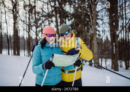 Ältere Paare, die sich während des Skilanglaufs im verschneiten Wald eine Karte ansehen. Stockfoto