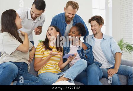 Fröhliche Freunde, die sich lustige Videos auf dem Smartphone-Bildschirm während freundlicher Treffen zu Hause ansehen. Stockfoto