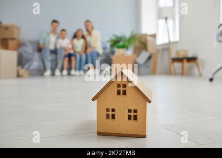 Kleines Holzhaus und Familie sitzen auf der Couch Umzug in neues Haus auf dem Hintergrund. Stockfoto