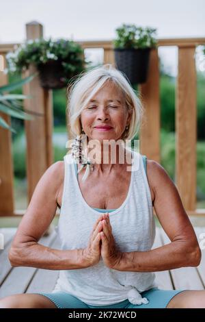 Eine ältere Frau, die im Sommer draußen auf einer Terrasse sitzt und Yoga-Übungen macht. Stockfoto