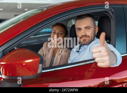 Glückliches junges Paar wählt und kauft ein neues Auto für die Familie im Autohaus Stockfoto