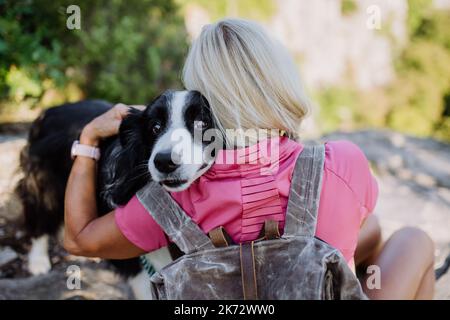 Ältere Frau, die sich ausruhte und ihren Hund umarmte, während sie im Wald spazieren ging. Stockfoto