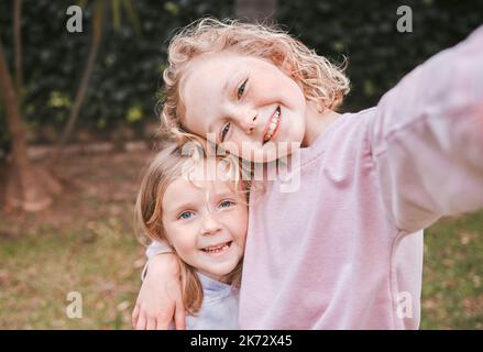 Wer braucht Spielzeug, wenn Sie glückliche Kindheitserinnerungen bekommen. Zwei entzückende kleine Mädchen, die Selfies in einem Garten machen. Stockfoto