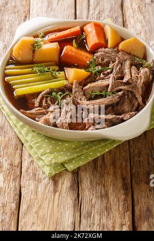 Köstlicher Rinderbraten mit Kartoffeln, Sellerie und Karotten mit Thymian und Rosmarin in der Schüssel auf dem Holztisch. Vertikal Stockfoto