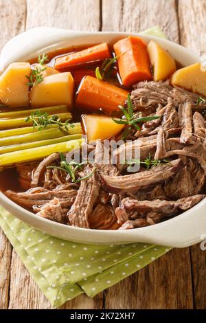 Hausgemachtes Slow Cooker Topfbraten mit Karotten, Sellerie und Kartoffeln in der Schüssel auf dem Holztisch. Vertikal Stockfoto