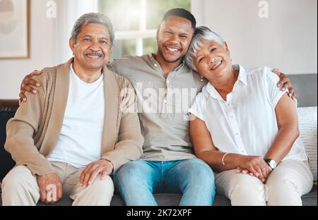 Meine Eltern, mein Schatz. Porträt eines reifen Paares, das sich mit seinem Sohn zu Hause auf dem Sofa verklebt. Stockfoto