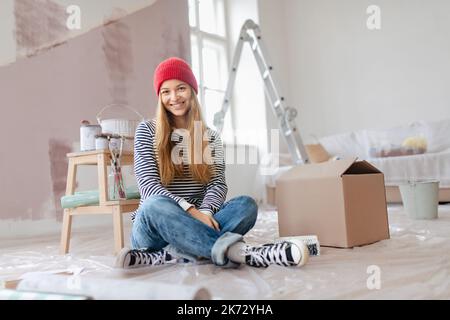 Glückliche junge Frau, die beim Malen von Wänden in ihrer Wohnung Pause machte. Denken Sie an neue Projekte. Konzept der Wiederverwendung von Materialien und nachhaltig Stockfoto
