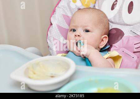 Nettes Baby Mädchen essen mit Löffel in der Küche Stockfoto