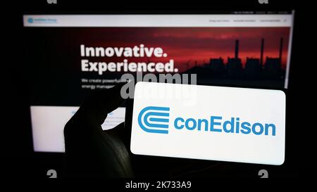 Person mit Mobiltelefon und Logo des US-Unternehmens Consolidated Edison Inc. (ConEdison) auf dem Bildschirm vor der Webseite. Konzentrieren Sie sich auf die Telefonanzeige. Stockfoto