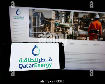 Person, die das Smartphone mit dem Logo des katarischen Mineralölunternehmens QatarEnergy auf dem Bildschirm vor der Website hält. Konzentrieren Sie sich auf die Telefonanzeige. Stockfoto