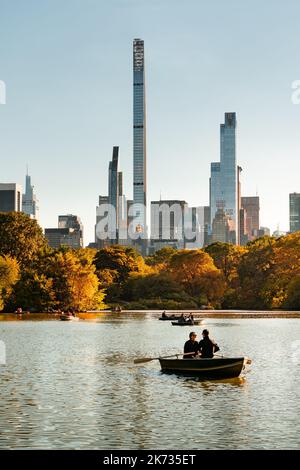 New York Central Park Lake im Herbst mit Ruderbooten und Blick auf die Wolkenkratzer der Milliardäre Row (Steinway Tower und One57). Midtown Manhattan Stockfoto