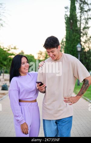 Zwei lateinische Freunde mit dem Smartphone und lachend auf der Straße. Stockfoto