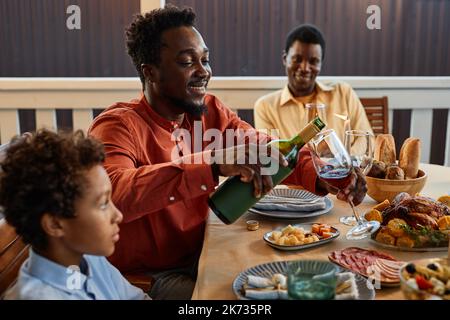 Seitenansicht Porträt eines afroamerikanischen Mannes, der Wein in Gläser gießt, während er die Dinnerparty im Freien genießt Stockfoto