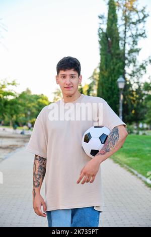Ein ecuadorianischer Mann, der mit einem Fußball posiert und auf der Straße lächelt. Stockfoto