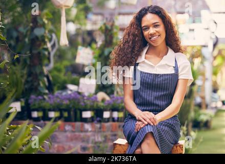 Bereit, Sie zum Lächeln zu bringen. Eine schöne junge Floristin, die in ihrem Garten sitzt. Stockfoto