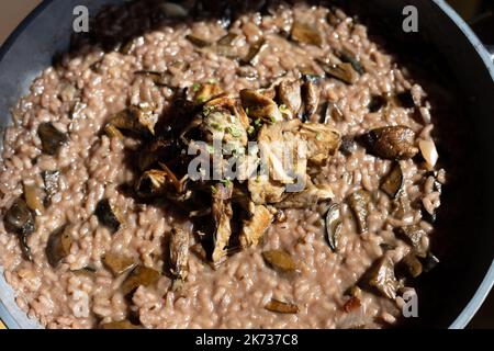 Rotes Risotto mit Wildpilzen in einer Schüssel, aus der ein mit gebratenem Sonnenschirm dekorierter Bolete besteht. Hochwertige Fotos Stockfoto