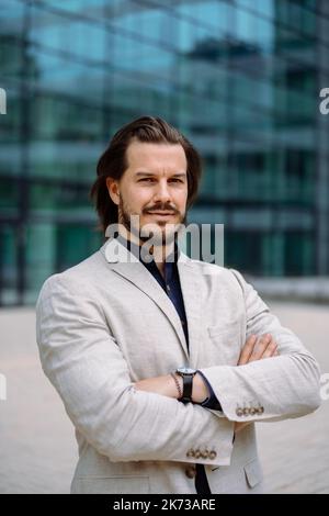 Lächelnder, positiv bärtiger Geschäftsmann in Anzug, der auf der Straße auf die Kamera schaut Stockfoto