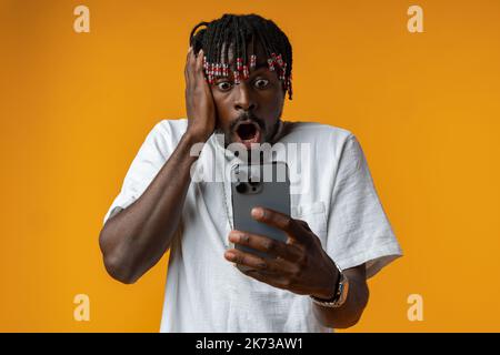 Junger afrikanischer Mann mit Smartphone über isoliertem gelben Hintergrund Stockfoto